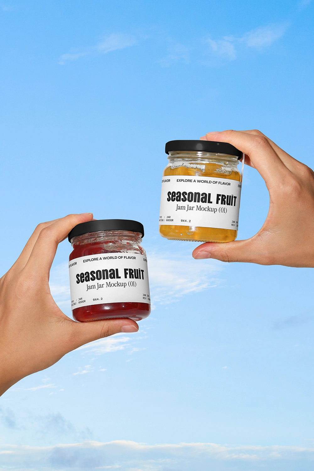 Hands holding two jam jars mockup with seasonal fruit labels against blue sky background
