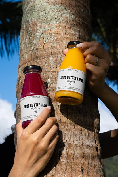 juice bottle label mockup with two handheld glass bottles outdoor scene