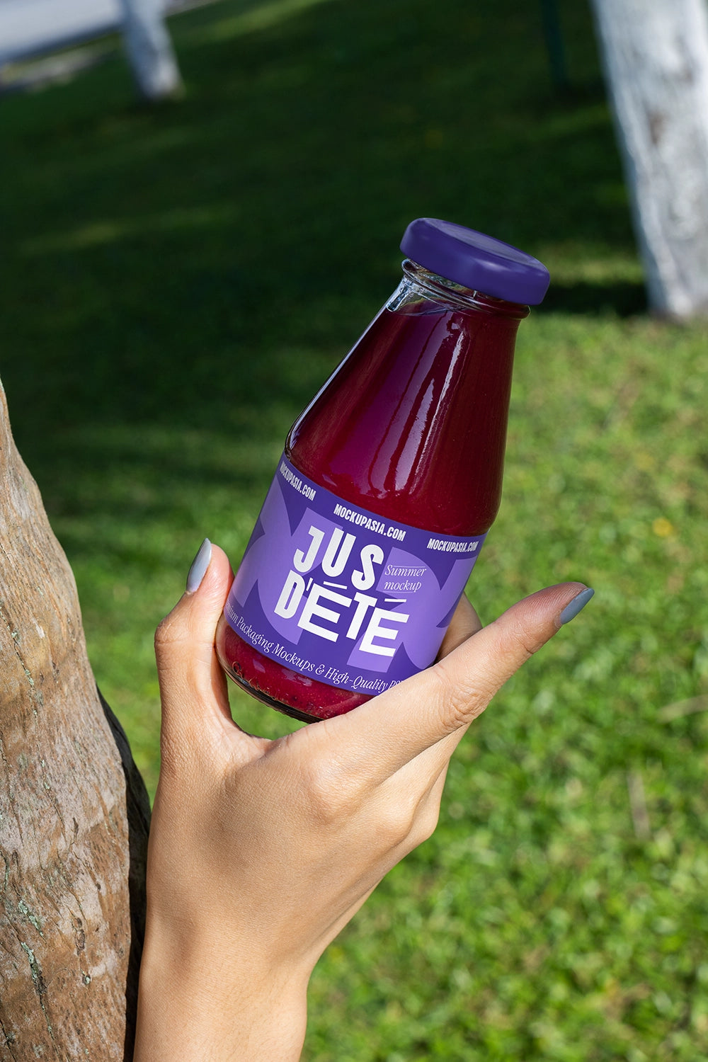 Red juice bottle mockup handheld on grass natural light organic drink branding template