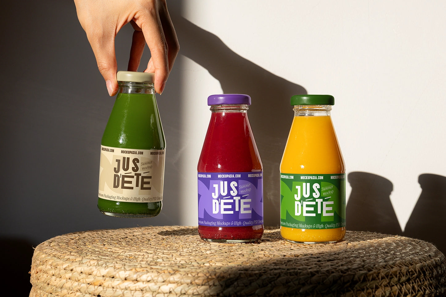 Glass juice bottle label mockup set with green, red and orange drinks on textured surface