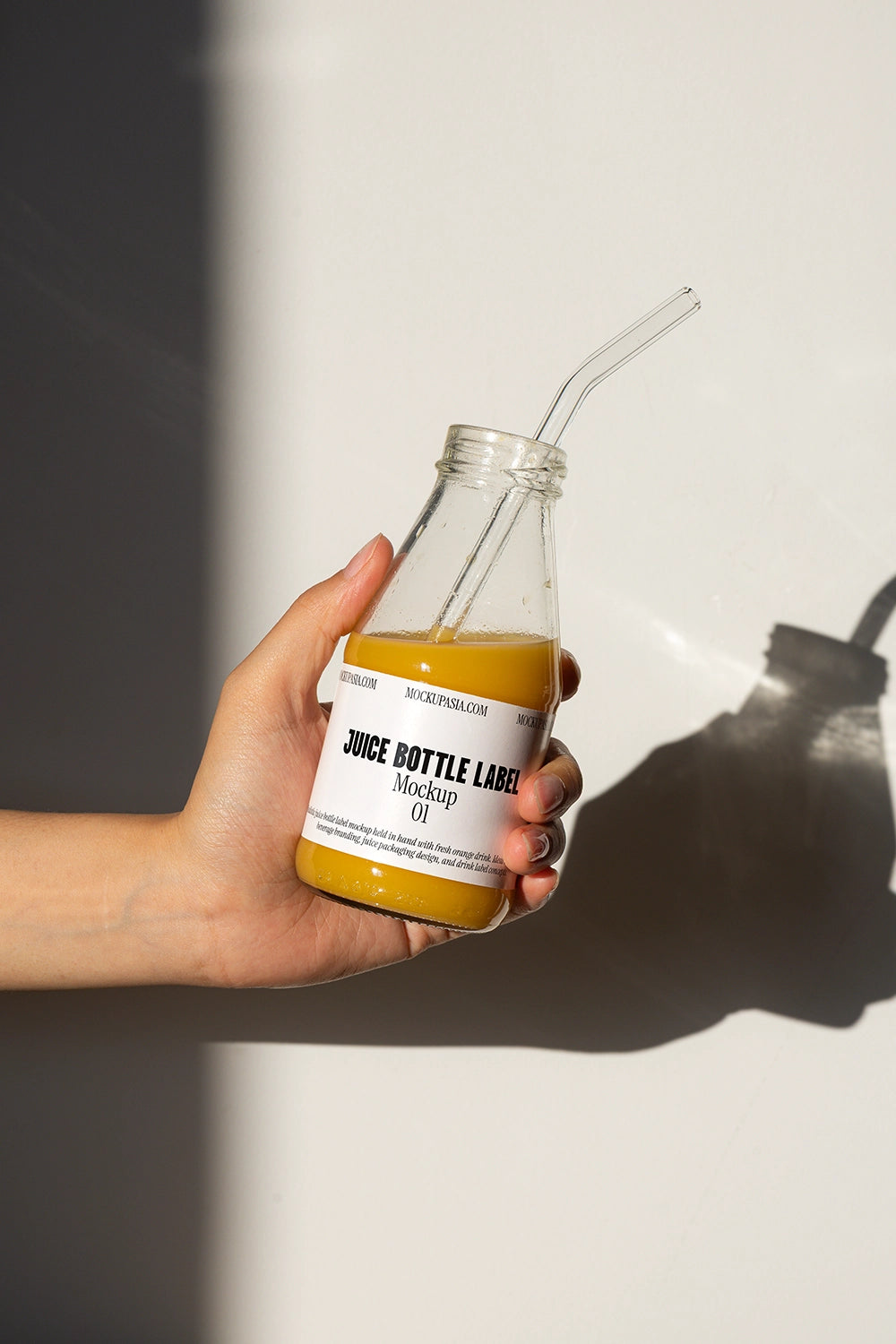 Hand holding glass juice bottle mockup with straw and orange juice in natural sunlight
