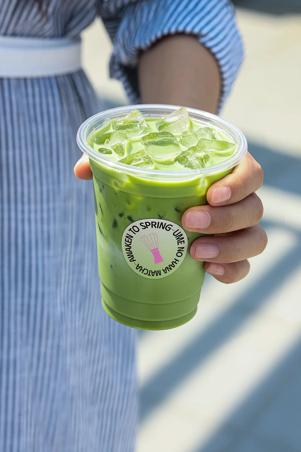 iced matcha latte in clear plastic cup held by hand, refreshing drink lifestyle scene