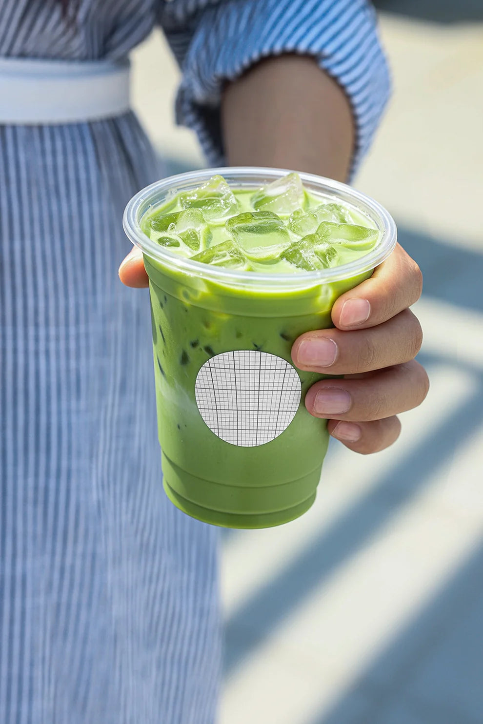 green matcha iced drink in plastic cup with branding sticker, outdoor lifestyle setup