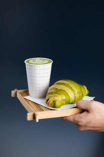 Realistic matcha paper cup mockup with green croissant on a bamboo serving tray