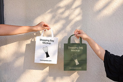 Paper shopping bag mockup PSD held by hands against sunlit wall