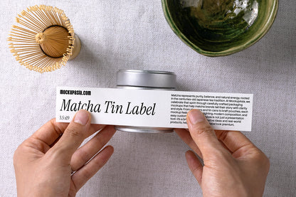 Matcha tin label mockup MCS13 showing hands applying a wrap label on a metal matcha tin in a top-down studio scene