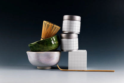 Premium matcha tin can mockup with stacked metal cans, ceramic matcha bowl, bamboo whisk, and dark studio background