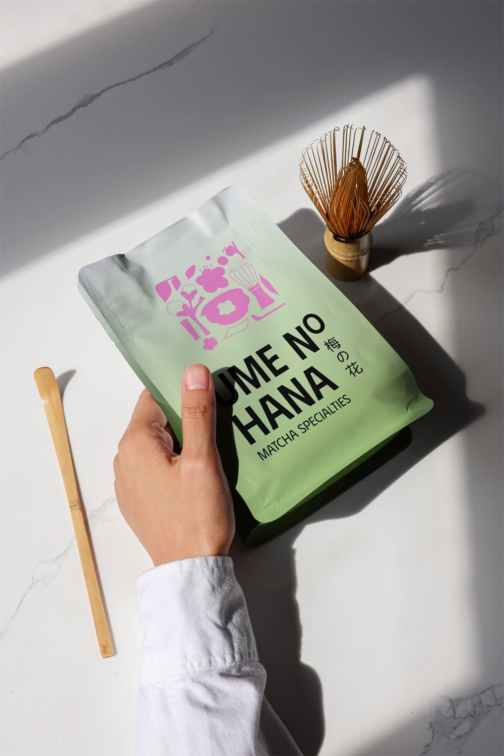 matcha pouch mockup held in hand with bamboo whisk and spoon, natural sunlight scene