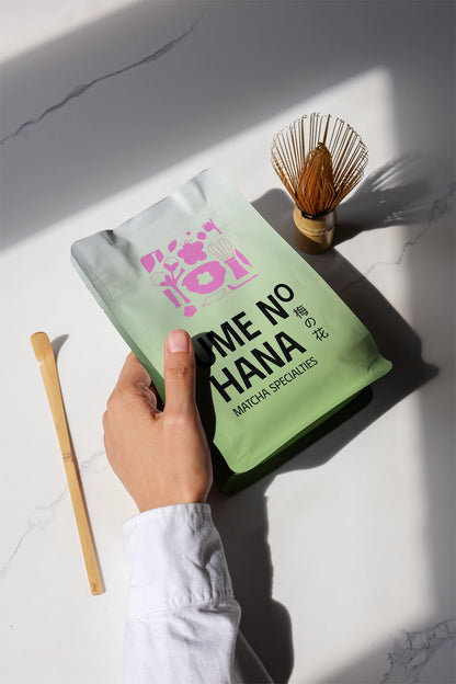 matcha pouch mockup held in hand with bamboo whisk and spoon, natural sunlight scene