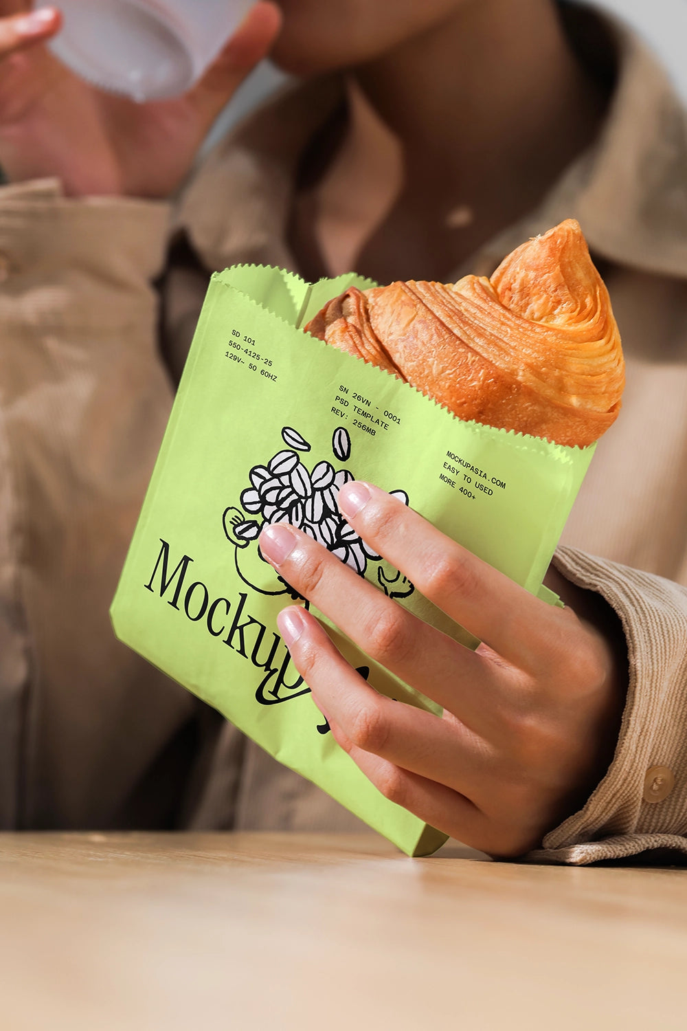 Person holding a green bag with a croissant, with a blurred background