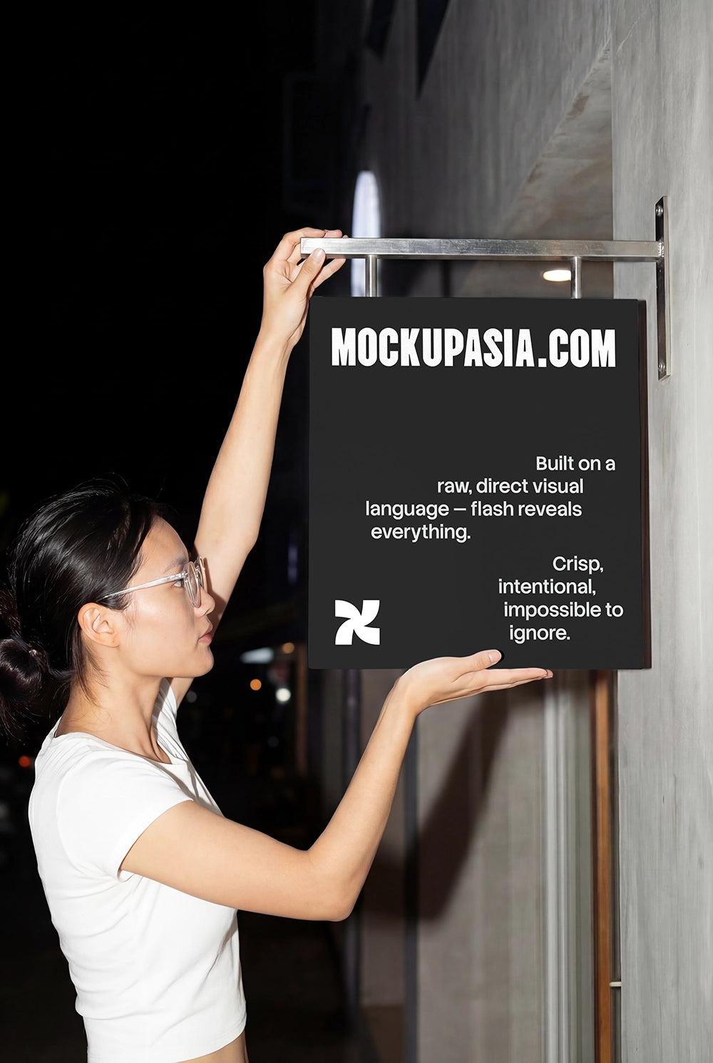asian woman installing a hanging storefront sign mockup at night with direct flash lighting