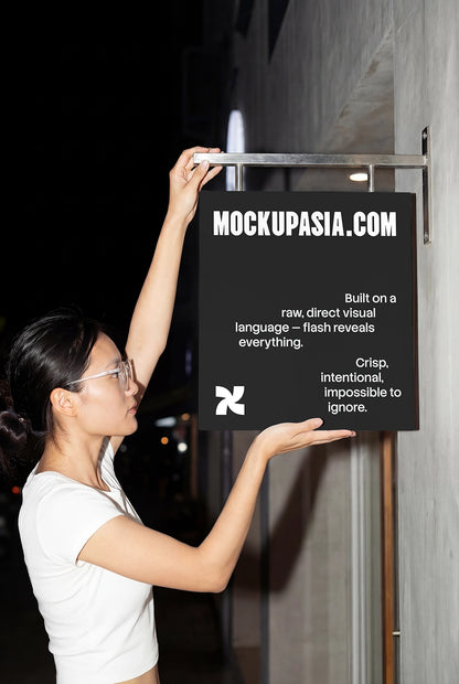 asian woman installing a hanging storefront sign mockup at night with direct flash lighting