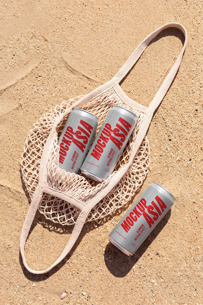 Three realistic aluminum sleek cans mockup in a mesh tote bag on sand