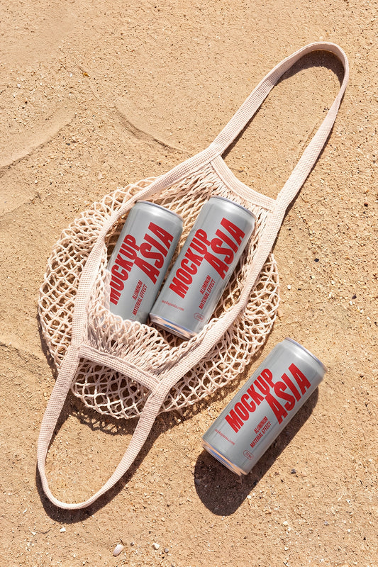 Three realistic aluminum sleek cans mockup in a mesh tote bag on sand