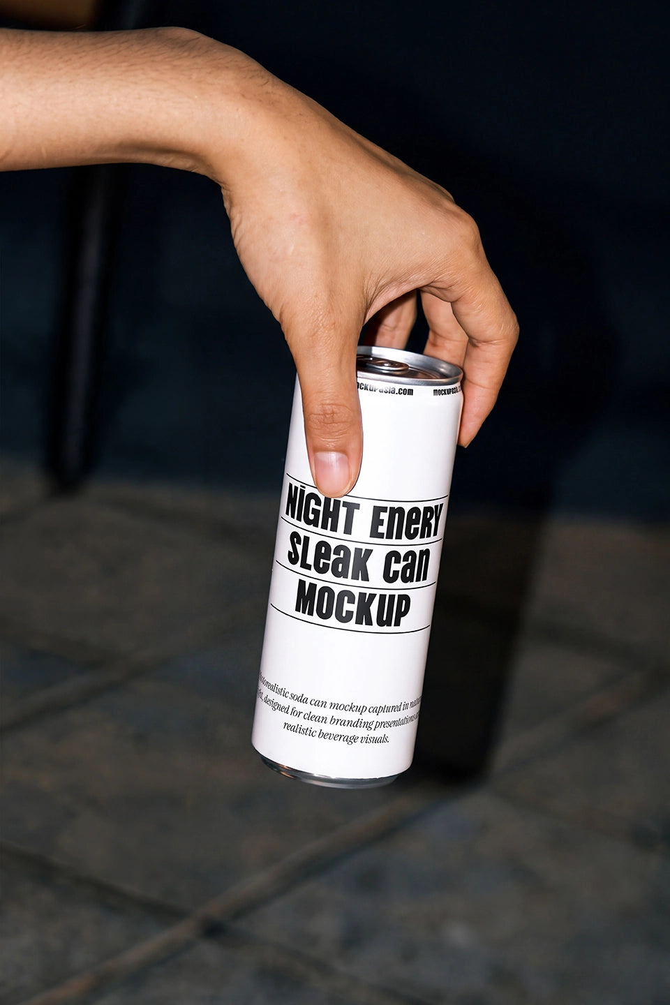 Sleek aluminum can mockup held by hand in a dark editorial setting.