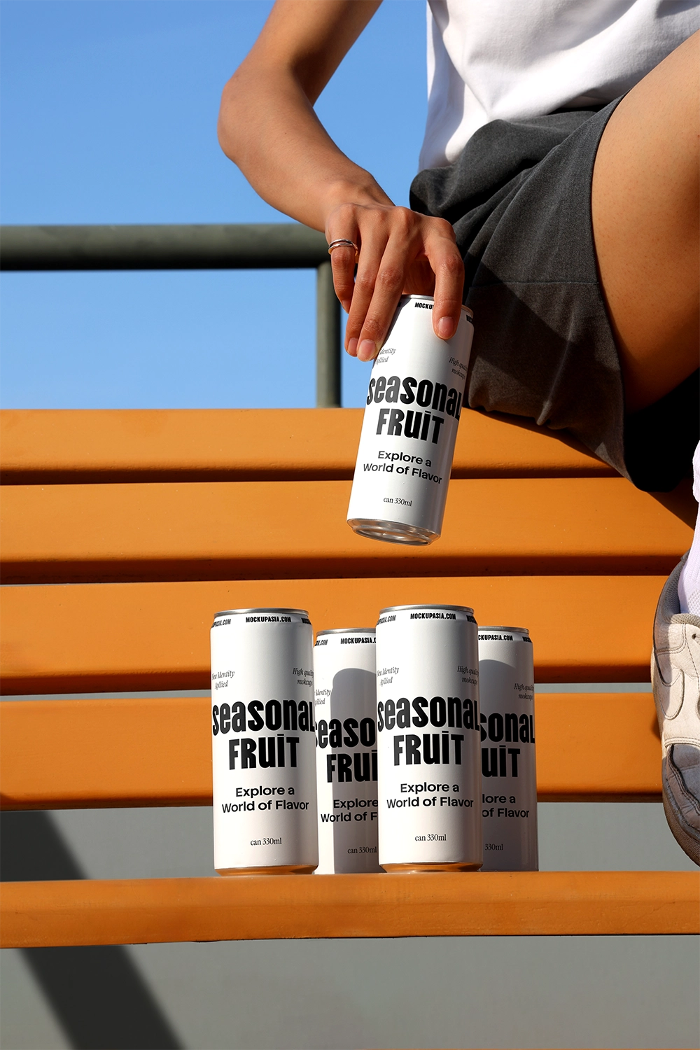 Soda can mockup on outdoor bench with hand holding can and multiple cans in sunlight lifestyle scene