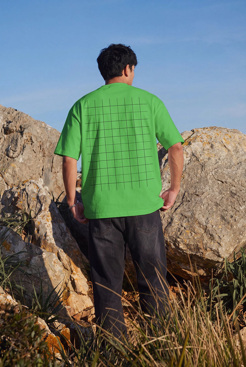 White oversized T-shirt back print mockup photographed among coastal rocks.