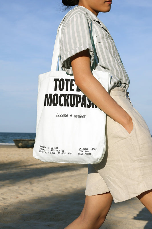 tote bag mockup carried on shoulder at beach with natural sunlight and ocean background