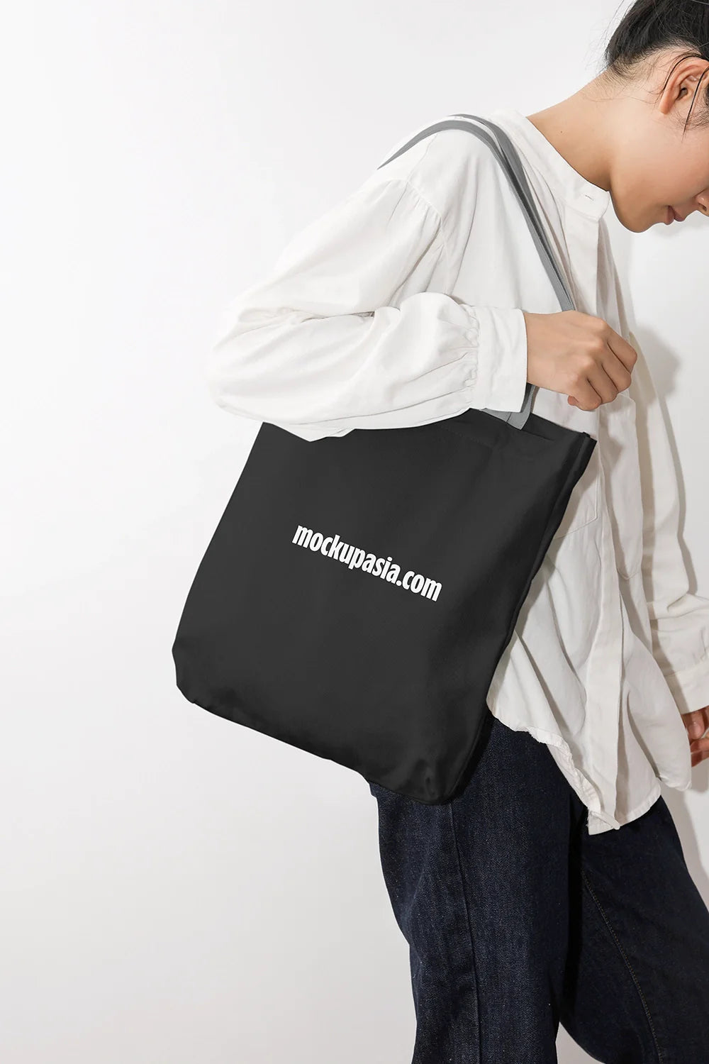 black canvas tote bag mockup on shoulder with clean studio background, minimal lifestyle scene