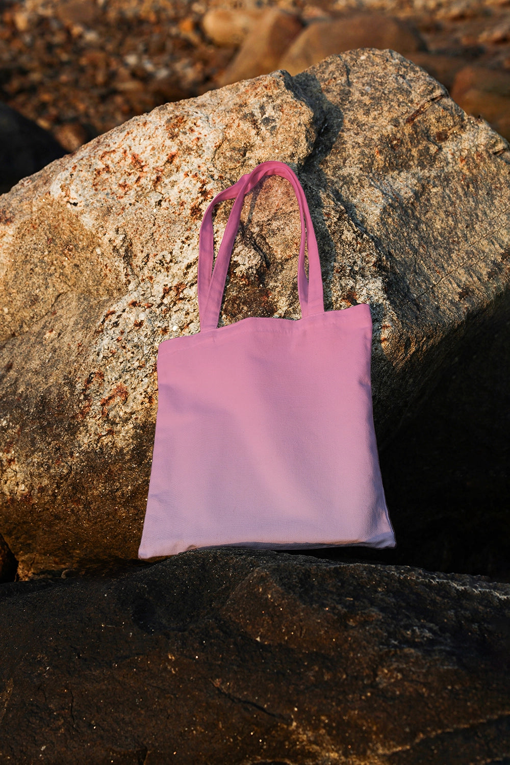 tote bag mockup placed on natural stone with warm sunlight, coastal branding presentation