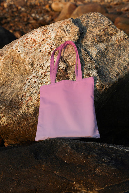 tote bag mockup placed on natural stone with warm sunlight, coastal branding presentation