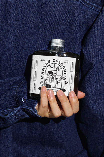 Hand holding cold brew bottle mockup with realistic lighting and denim background
