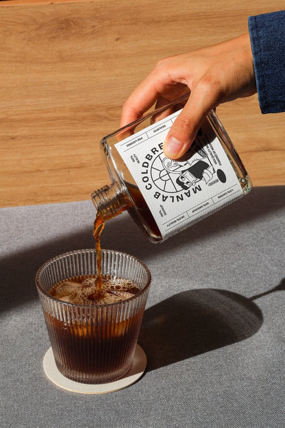 Cold brew coffee bottle mockup pouring drink into glass in lifestyle scene
