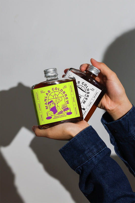 Cold brew bottle mockup with two bottles showing label color variation in hand
