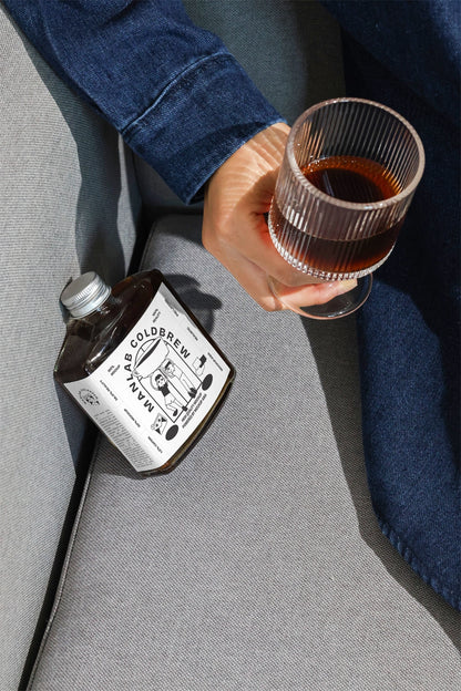 Cold brew bottle mockup with hand holding coffee glass in lifestyle scene
