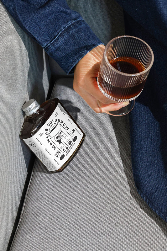 Cold brew bottle mockup with hand holding coffee glass in lifestyle scene
