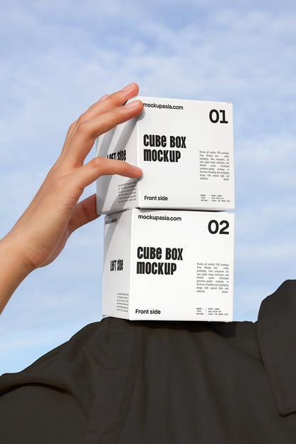 Cube box mockup with two stacked packaging boxes held by hand against sky background