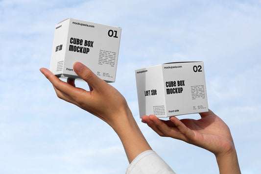 Cube box mockup with two packaging boxes held in hands against blue sky background