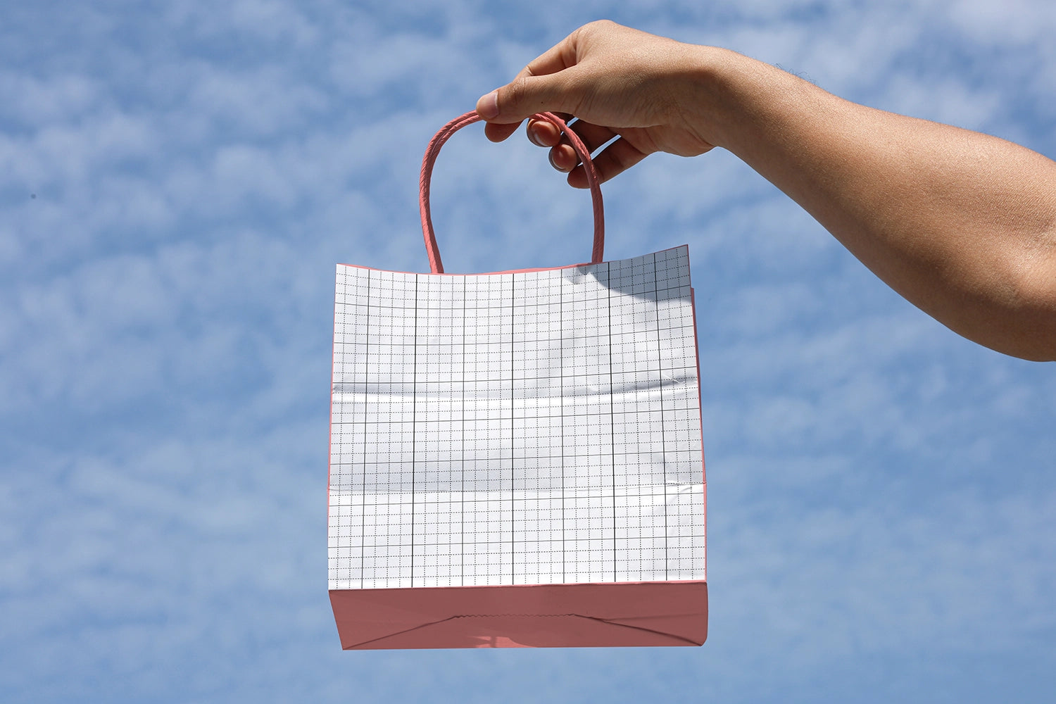 minimal paper bag mockup outdoor with hand holding bag clean sky backdrop branding scene