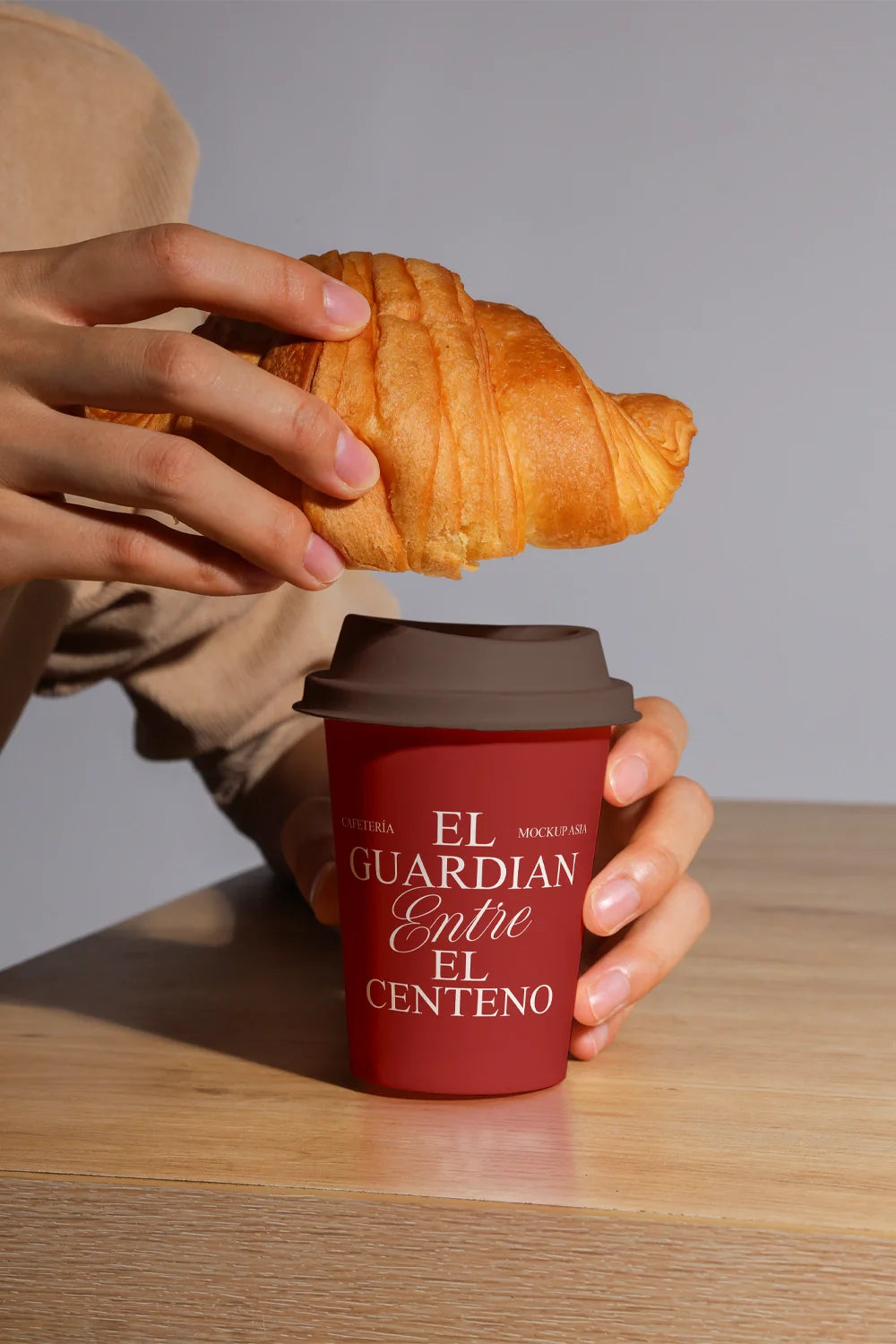 paper coffee cup mockup with croissant being placed on top, realistic hand interaction