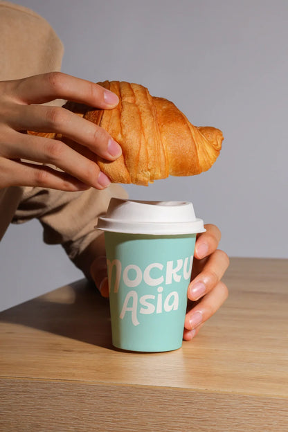 coffee cup mockup on wooden table with pastry and hands, bakery lifestyle scene