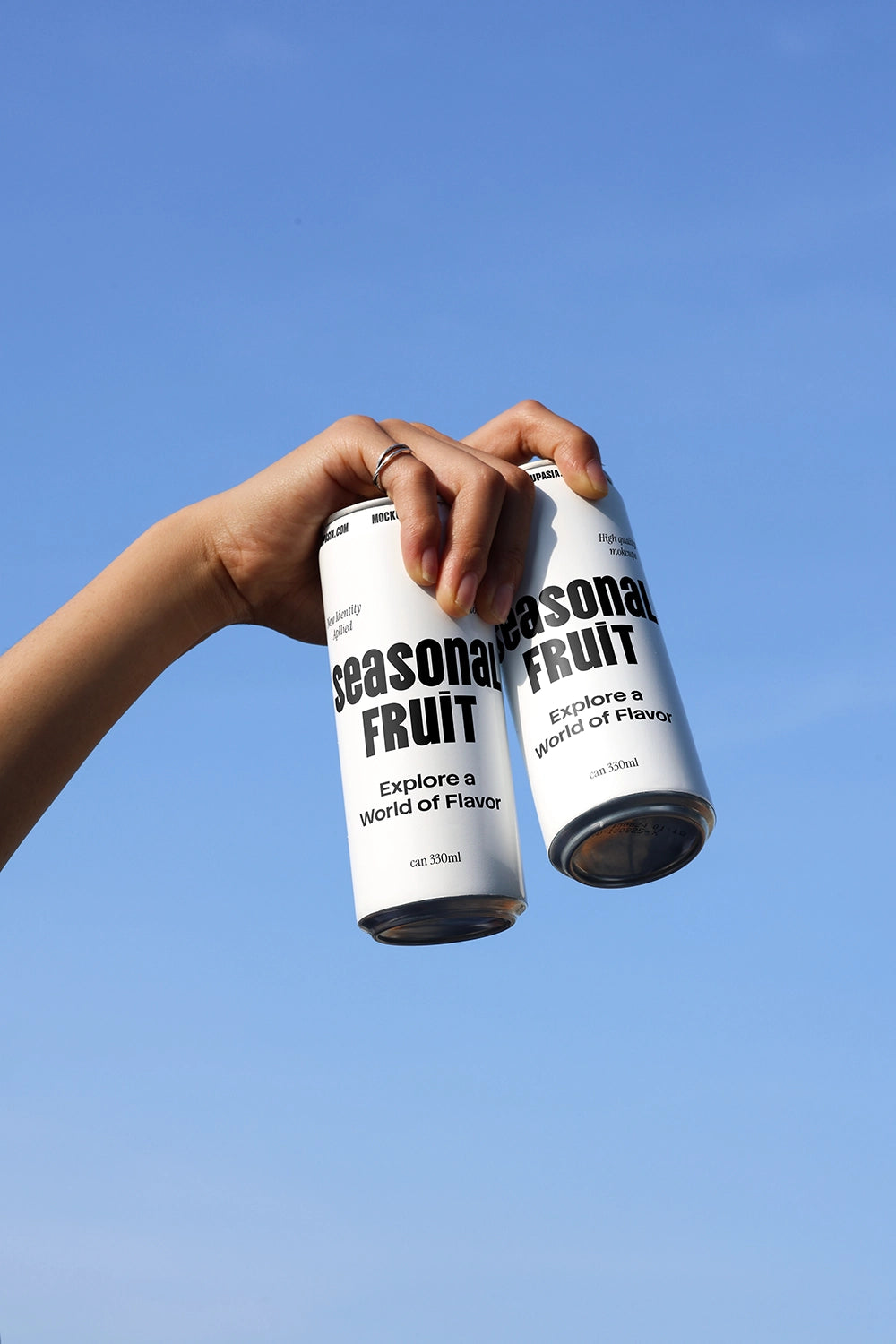Dual soda can mockup held by hand against blue sky showing beverage packaging variations